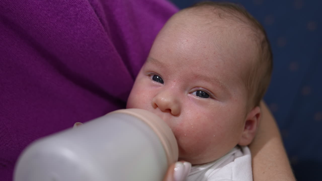 Adorable newborn baby being fed from the bottle. Mother holding her child in arms and feeding it from the bottle. Close up.