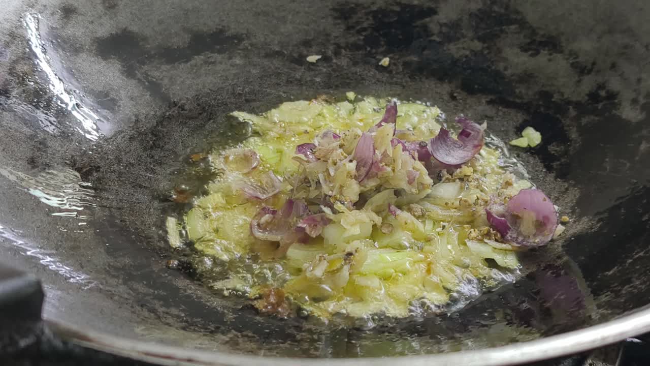A chef is sautéing sliced onions in a hot wok using palm oil, creating a wonderful, savory aroma. The cooking process is a key step in preparing an appetizing meal