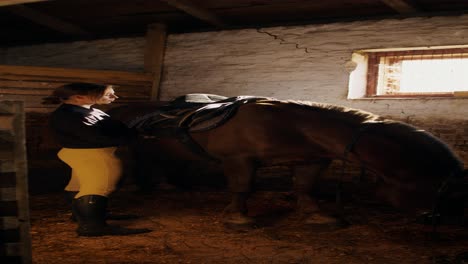 mujer preparando un caballo para montarlo en un establo