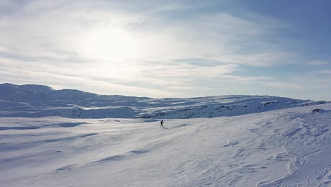 Aerial-flying-along-person-silhouette-skiing-on-snow-covered-mountain-top---wide-overview-shot