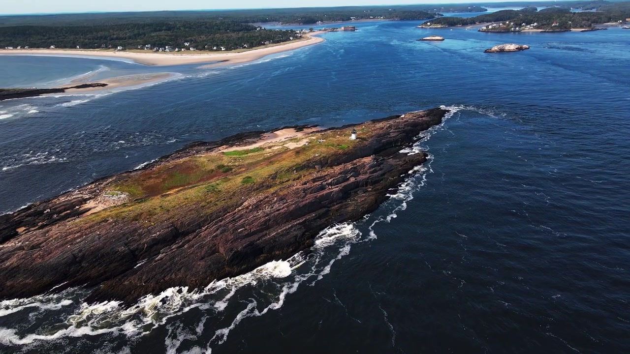 Epicki widok z lotu ptaka zbliżający się do historycznej latarni morskiej Pond Island na małej wyspie w pobliżu Popham Beach, Maine, z latającymi mewami i falami rozbijającymi się o skalistą wyspę u ujścia rzeki Kennebec