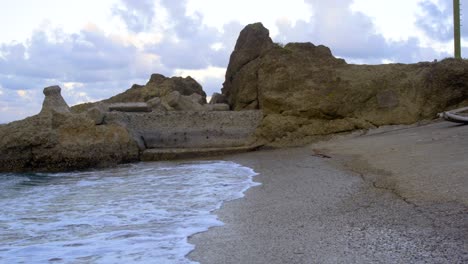 white foamy waves gently crashing on empty concrete boat ramp on rocky shoreline with cloudy sky in background, filmed as stationary establishing shot