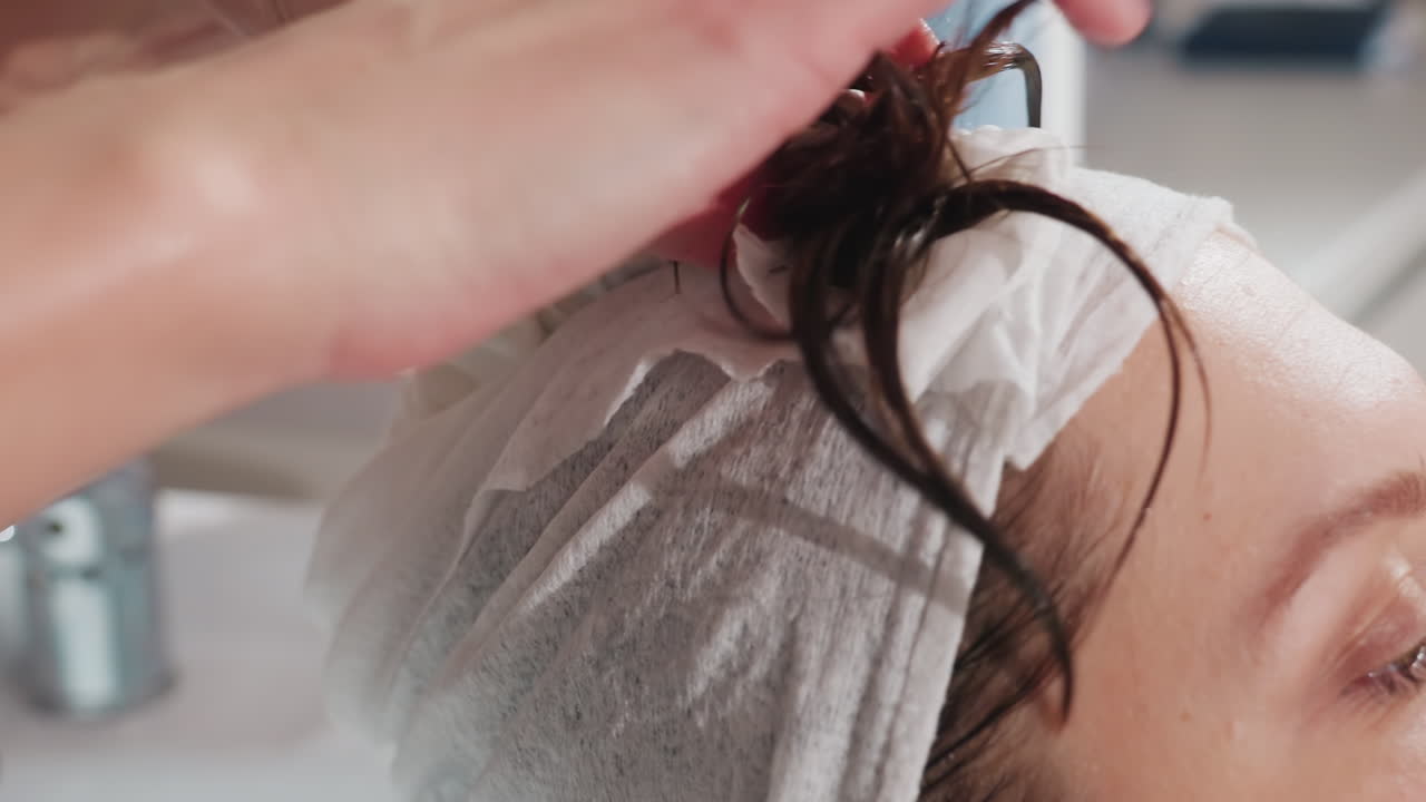 미용실 의자에 앉아 일회용 캡을 쓰고 있는 백인 여성, 시술 전에 보호용 헤드 커버를 고정하는 어시스턴트, 클로즈업된 손, 깨끗하고 현대적인 싱크대 공간, 부드러운 자연광, 차분하고 전문적인 분위기