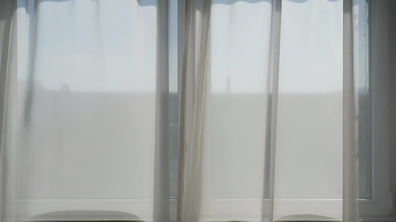 Shifting sheer curtains swaying from breeze through window in room, changing light on sill