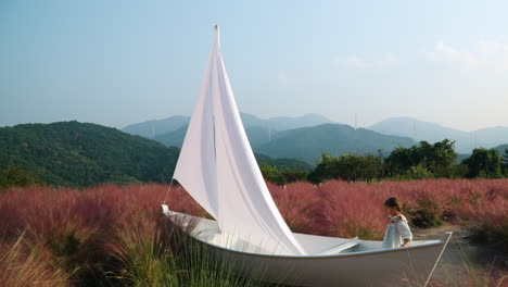 little girl playing inside wooden sail boat at pink muhly grass field - herb island