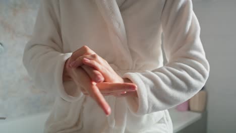 unrecognizable woman in bathrobe applying moisturizing cream on hands.