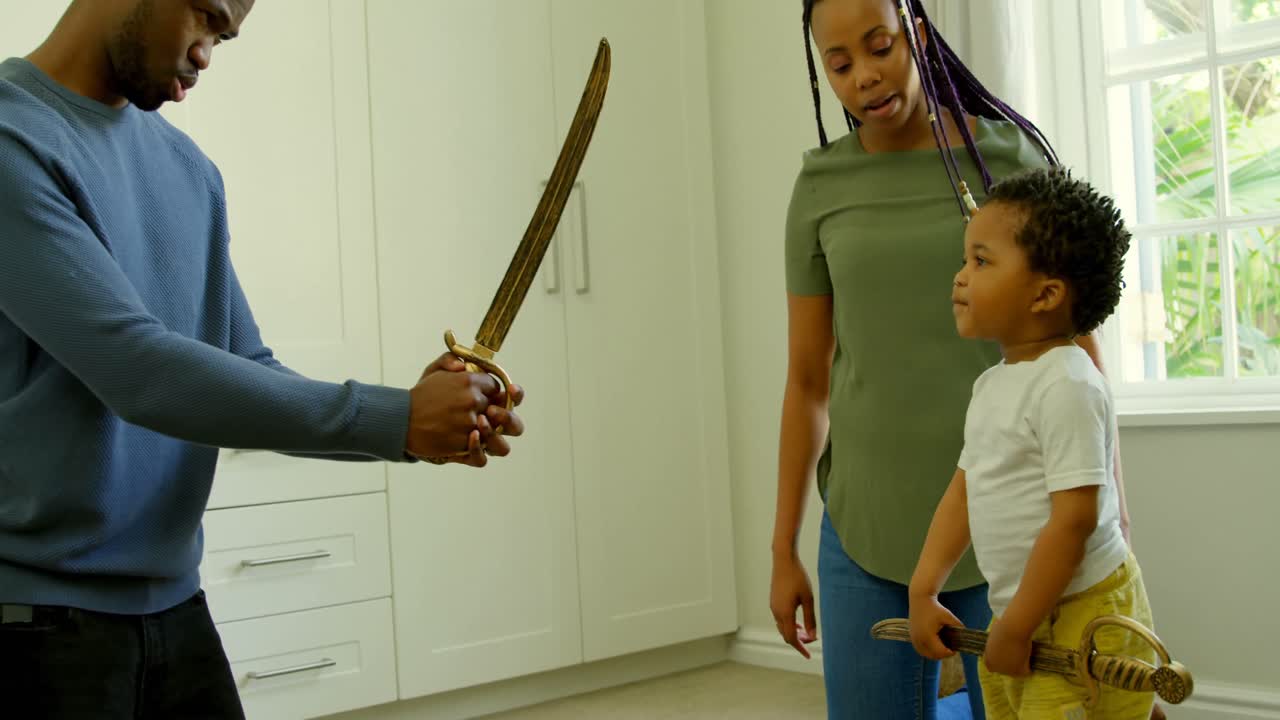 Side view of young black father and son playing with toy sword in a comfortable home 4k