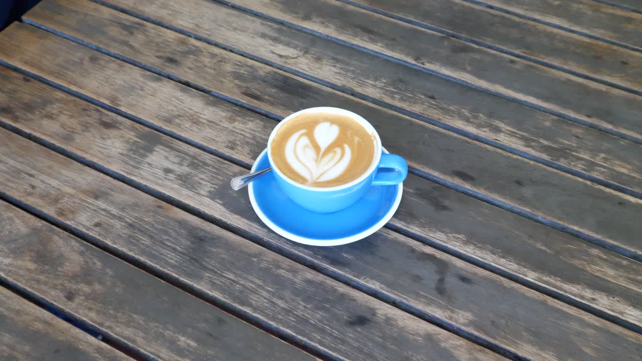 A person and a blue cup of delicious cappuccino on a wooden table at a coffee shop for breakfast