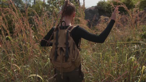 chica viajera con mochila caminando por la hierba alta en una isla tropical y mira a su alrededor