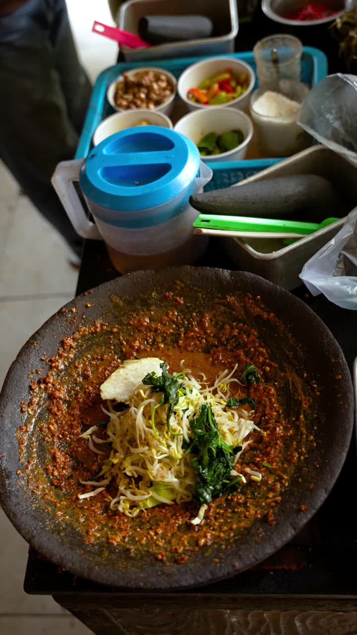 Lotek salad mixed in a stone mortar with peanut sauce, sprouts and greens; vertical static close-up
