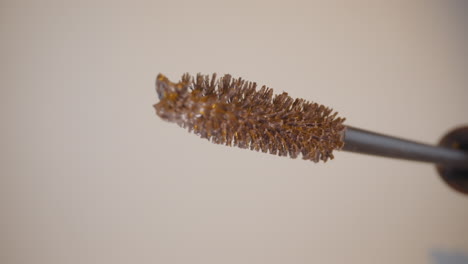 mascara wand soaked in pastel liquid on beige background