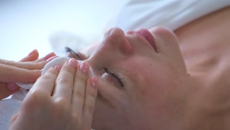 Close-up face of relaxed woman having shoulder massage from professional massage therapist during wellness treatment at spa center. Happy redhead female enjoying moment of wellness and relaxation.