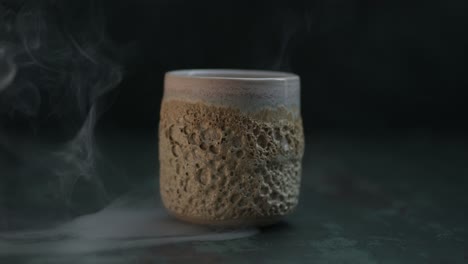 smoke enveloping a standing ceramic cup with a coral texture on the dark background