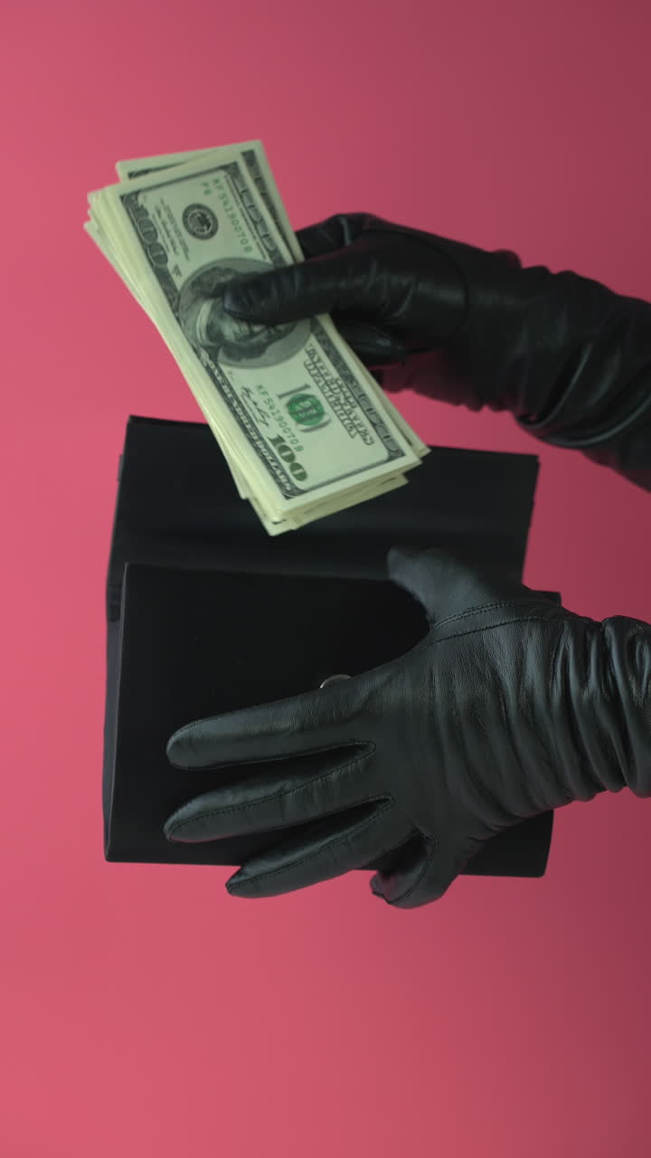 Mani guantate che prendono una pila di banconote da cento dollari da una pochette