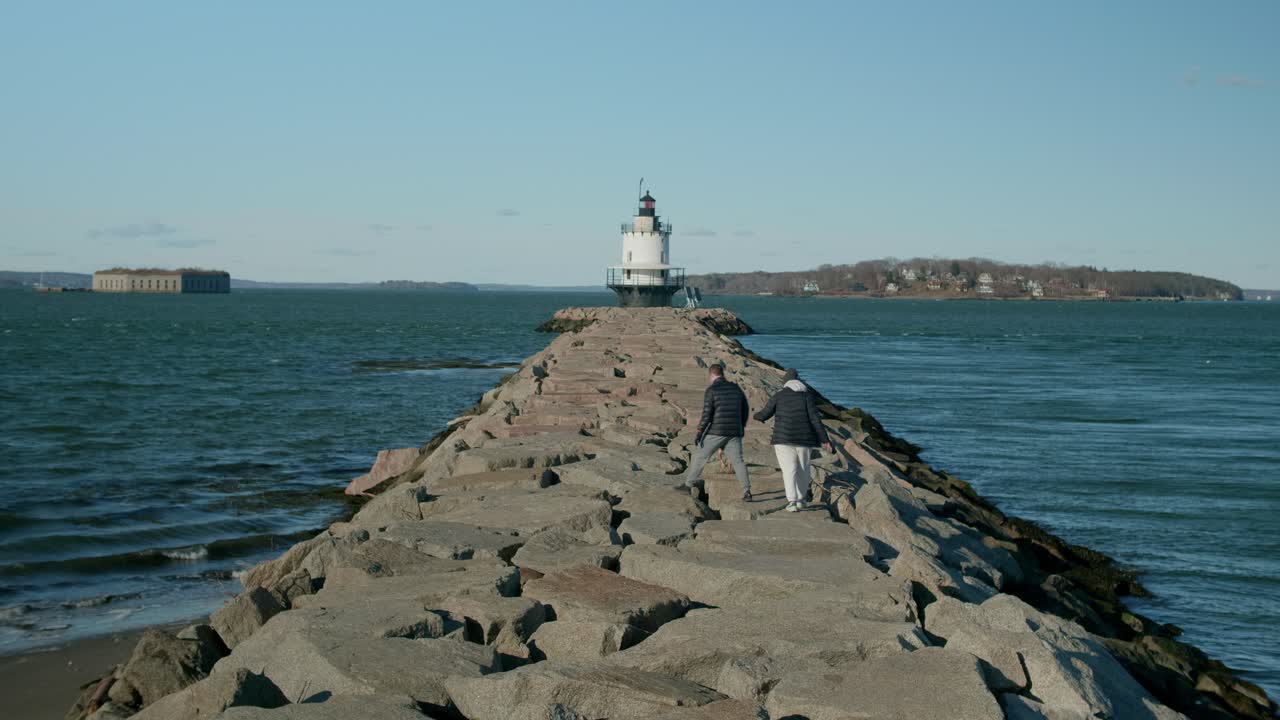Two People Walking With A Dog On Breakwater Toward The Spring Point Ledge Lighthouse In South Portland, Maine, United States. static shot