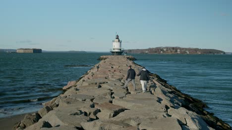 two people walking with a dog on breakwater toward the spring point ledge lighthouse in south portland, maine, united states. static shot