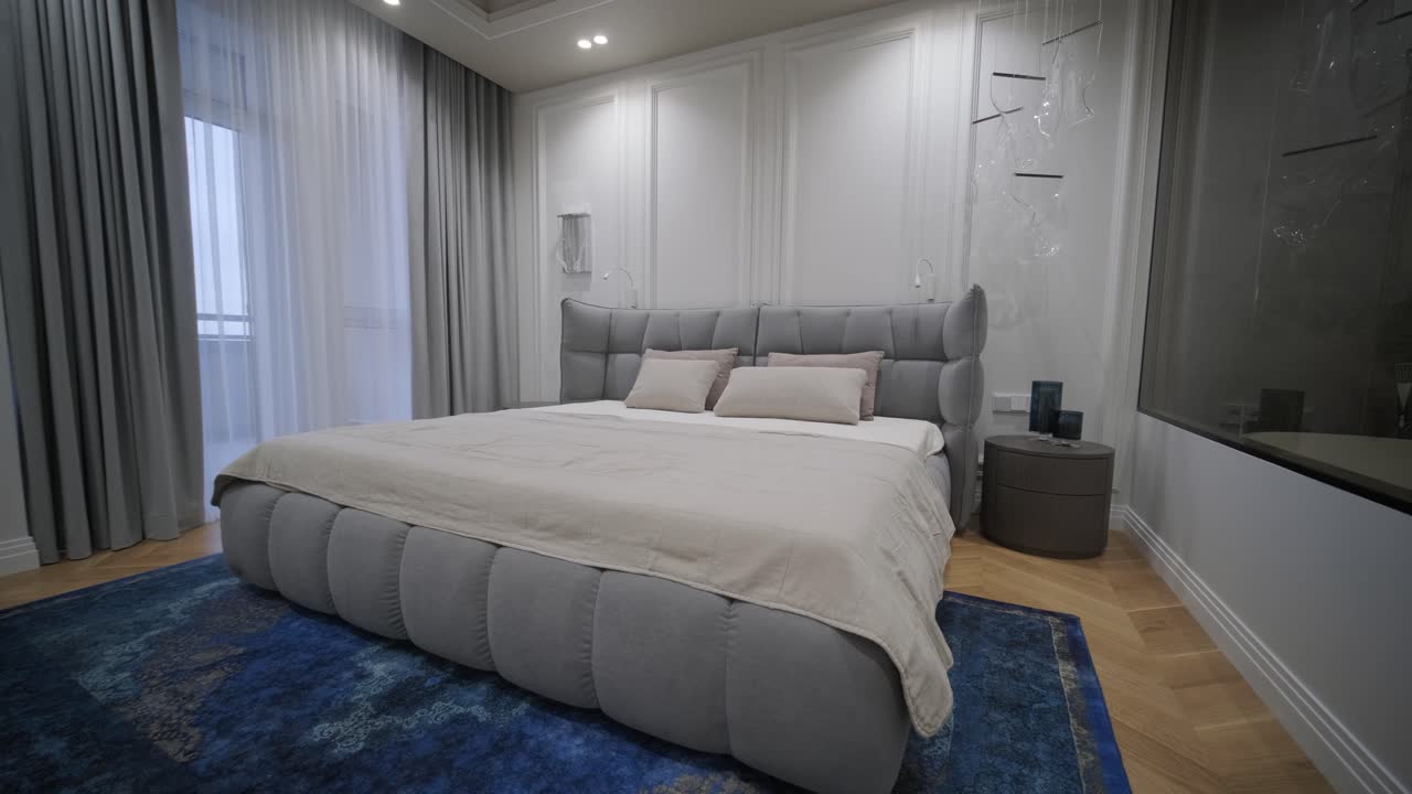 Elegantly designed bedroom with a large, tufted bed, rich blue rug, classic panel walls, and a clear view into a sleek, modern en-suite bathroom, reflecting a luxurious and harmonious living space.