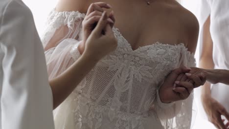 bride girlfriends bridesmaids in dressing gown helps the woman to put on wedding dress, holding hand