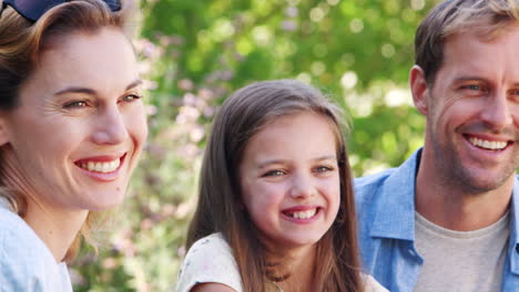padres sonrientes y hija joven sentada en el jardín