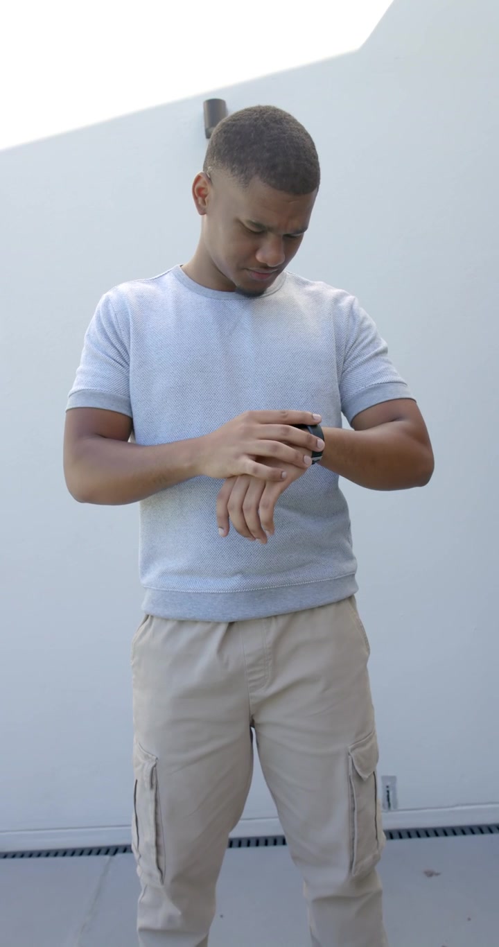 Vertical video: African American man raising wrist, tapping smartwatch and checking watch on patio