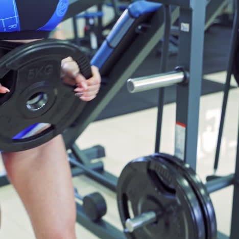 athletic woman with slim body in blue shorts is putting disk to the barbell. sports gym background and a young woman training.