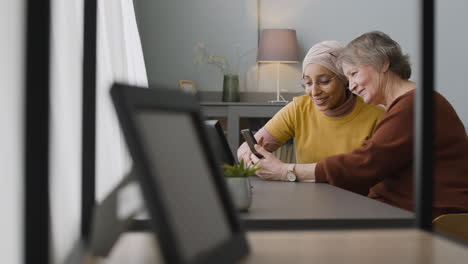 Mujer-árabe-Enseñando-A-Una-Anciana-A-Usar-Un-Teléfono-Inteligente-En-Casa