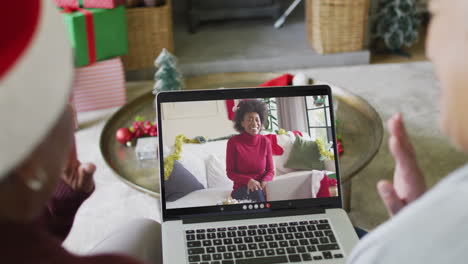 diversas amigas mayores agitando y usando una computadora portátil para una videollamada de navidad con una mujer en la pantalla