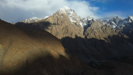 cinematic aerial shot of tupopdan peak, passu cones in hunza pakistan, snow covered mountain peaks with steep cliffs, wide revealing drone shot