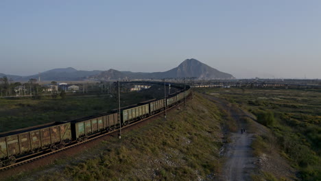 follow up aerial shot of full loaded coal cargo train locomotives pulling long carriage train approaching the intersection of the railways, on the sunset