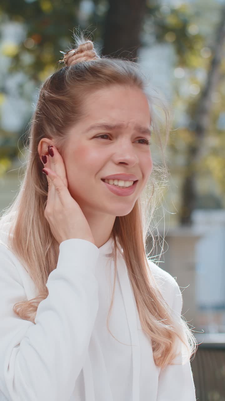 Sick young woman girl teenager suffers from ear pain while sitting on chair in city town street