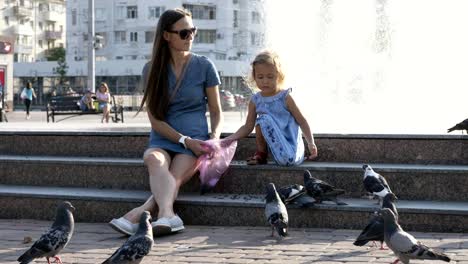 mother and daughter feedings street pigeons in the park at summer day 4k slow