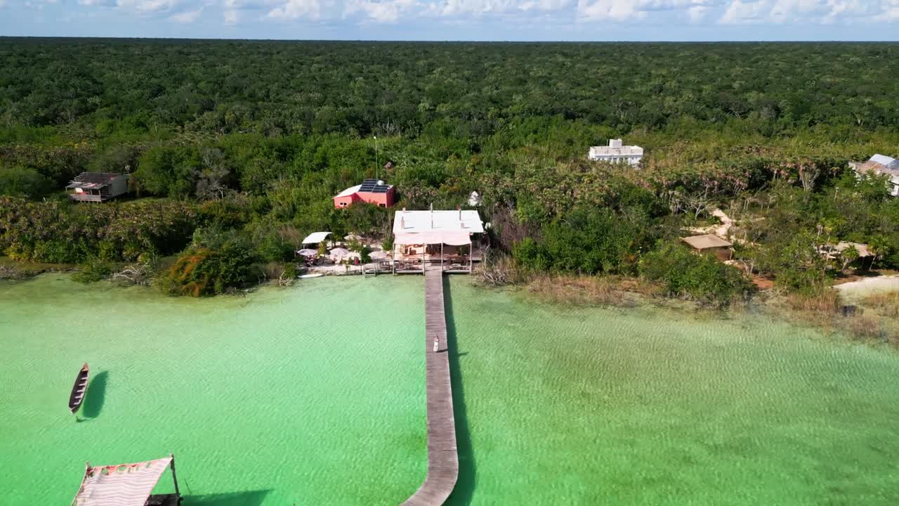 Drone stiger op og trækker sig tilbage for at afsløre en ung kvinde, der står på en lang træmole over lavt turkist vand nær Neek, Tulum, Quintana Roo, Mexico, omgivet af mangrover og tropisk kystlinje.