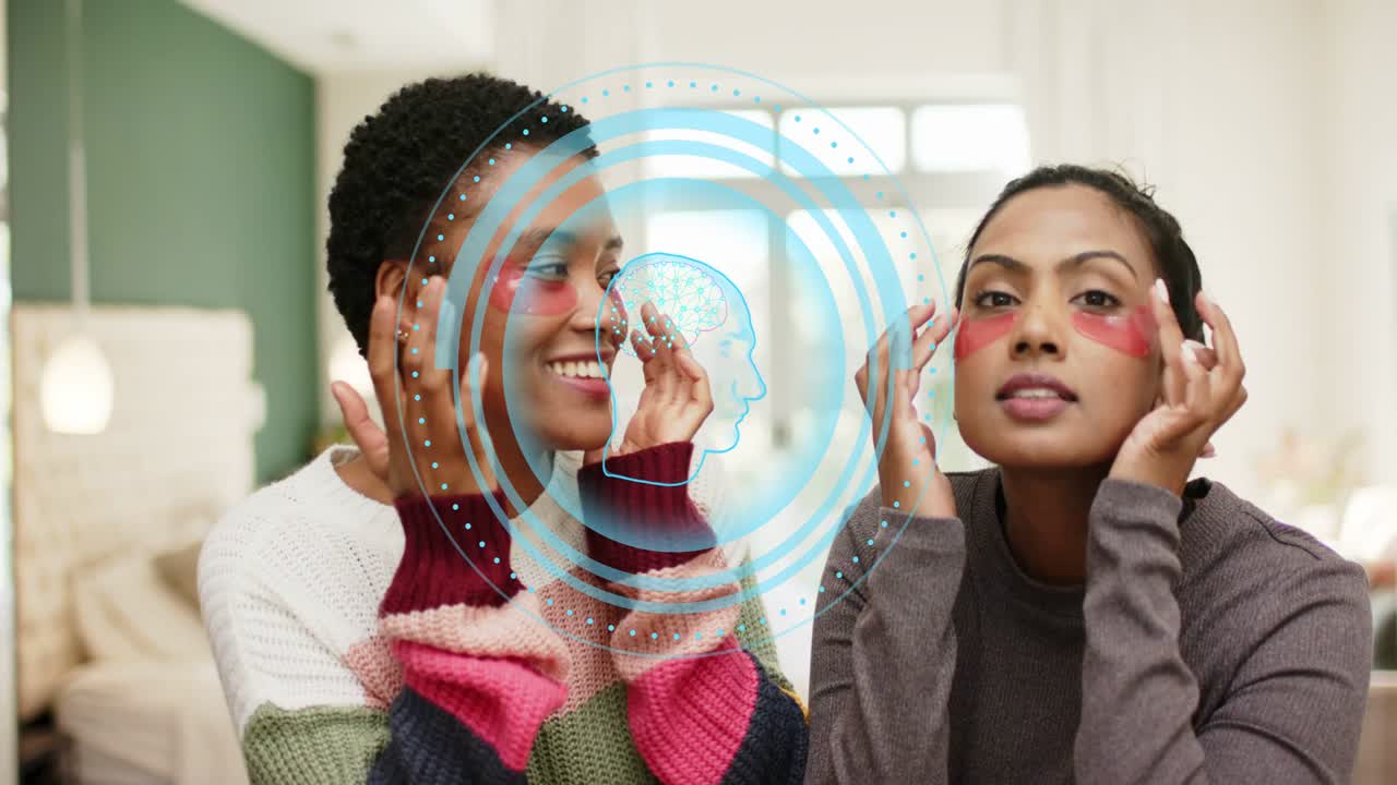 Two women on sofa placing pink eye patches adjusting blue overlay appearing over faces for skincare