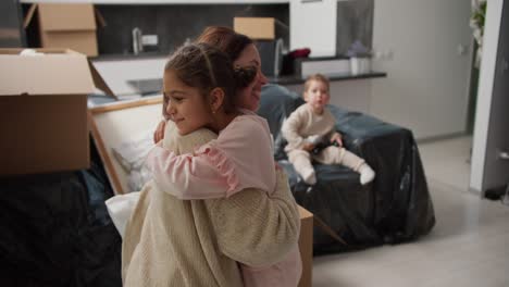 Happy-little-girl-in-pink-clothes-runs-to-her-brunette-mom-in-a-beige-sweater-and-hugs-her-then-hugs-her-dad-in-a-modern-apartment-after-moving.-Happy-children-rejoice-in-moving-to-a-new-apartment-with-their-parents-and-hugging