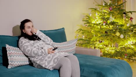 a woman is watching television sit on a couch near glowing christmas tree