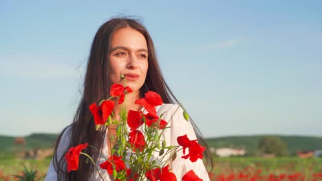 caucasian female holds vibrant colorful red wild poppy bouquet flowers and smells petals on sunny day, close up portrait