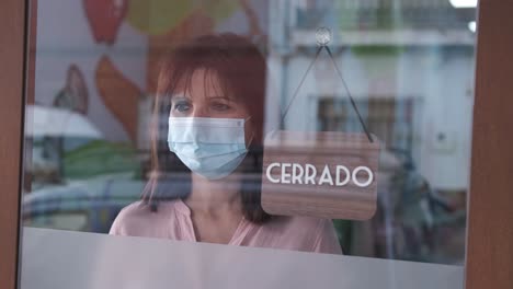 happy woman with face mask changing closed to open sign in spanish. start-up at covid time concept