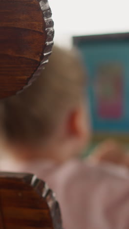 blurry view of little girl watching video via tablet computer at table in restaurant at eco resort focus on wooden chair back slow motion