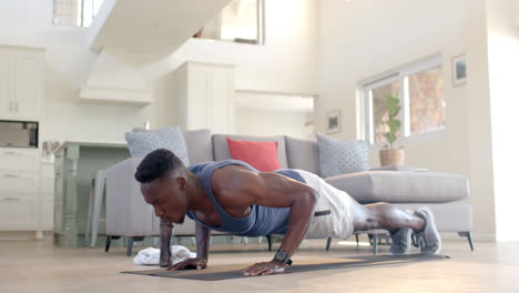 un hombre afroamericano concentrado haciendo flexiones en una sala de estar soleada, en cámara lenta.