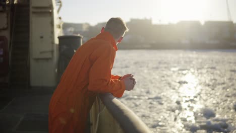 young man in orange uniform traveling on board of the ship in winter.