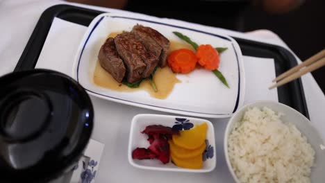 person eating steak, vegetables, rice, and miso soup