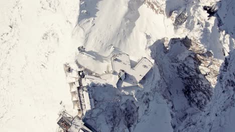 antena de arriba hacia abajo de un gran edificio en la cima de una cumbre nevada de una montaña en los alpes