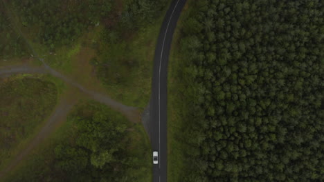 Vogelperspektive-Aus-Der-Luft-Von-Oben-Nach-Unten-Schwenkansicht-Des-Autos,-Das-Auf-Der-Straße-Durch-Den-Wald-Fährt.-Blick-Durch-Spärliche-Wolken.-Irland