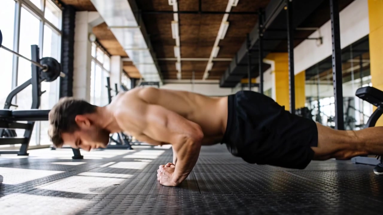 Starting shirtless male doing knee-to-plank lowering chest on rubber gym floor for conditioning