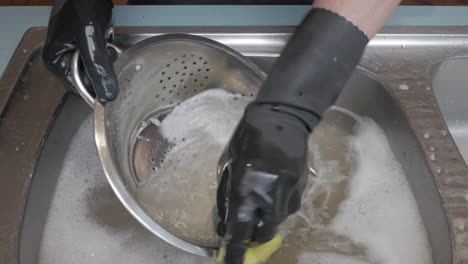 While-male-washing-a-chrome-colander-in-a-sink