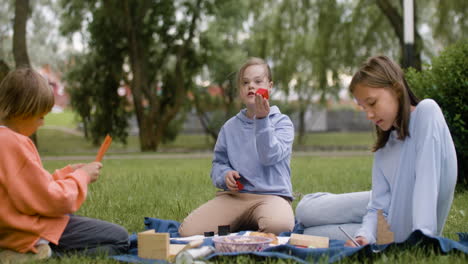 Kleines-Mädchen-Mit-Down-Syndrom-Beim-Basteln-Und-Reden-Mit-Ihren-Freunden,-Die-Im-Park-Sitzen