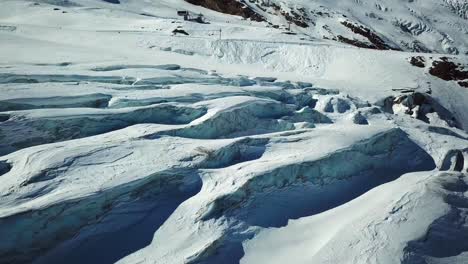 Blue-glacier-with-crevices-in-the-swiss-alps,-ski-slope-in-the-background