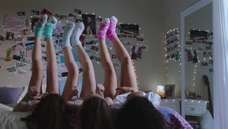 happy teen girls lying on bed at home with legs up having fun wiggling feet hanging out wearing pajamas enjoying relaxing morning on weekend