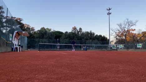 A-couple-demonstrates-their-tennis-technique-on-a-red-ground-court,-with-the-woman-executing-a-perfectly-executed-amortie-shot-as-the-man-looks-on-in-admiration