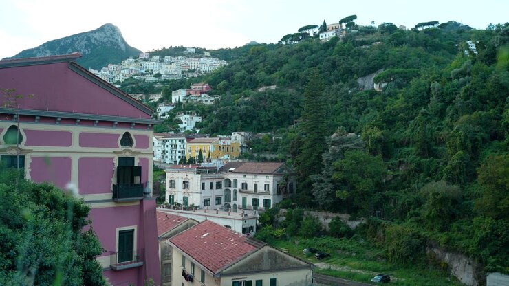 Casas em encostas em camadas erguem-se acima de edifícios coloridos da cidade e encostas verdes densas em Vietri, Itália, ao anoitecer